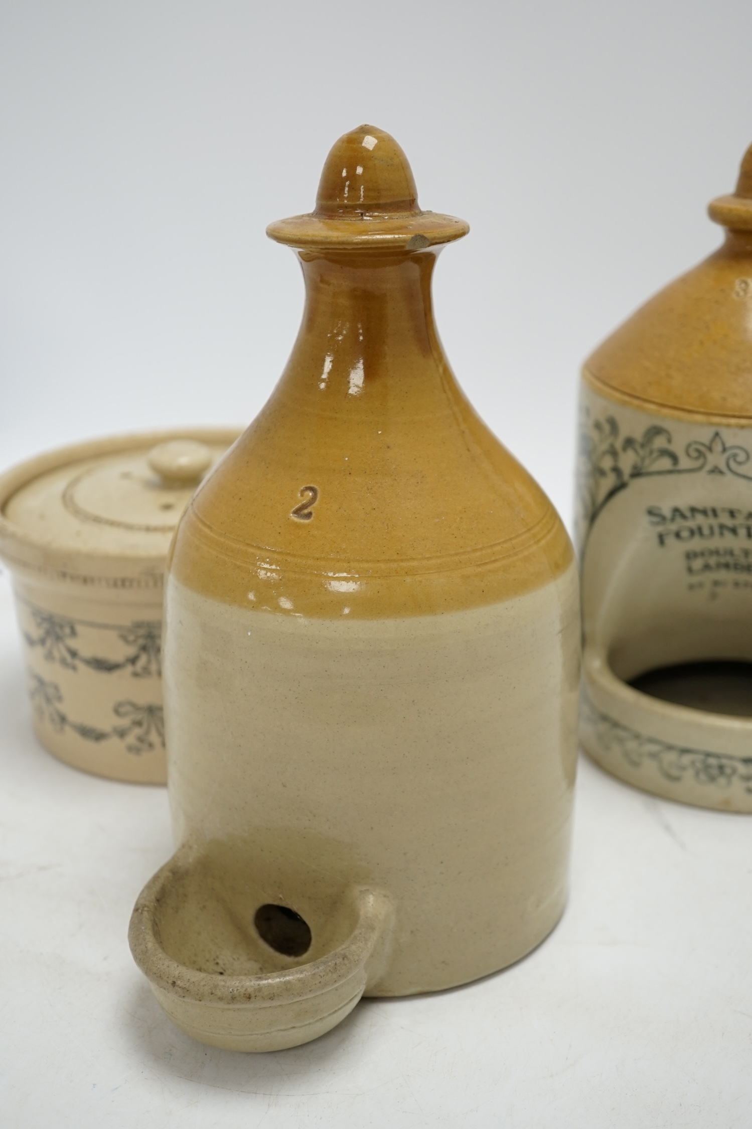 A late Victorian Doulton Lambeth Sanitary Fountain feeder, another similar, and a circular jar and cover, sanitary feeder 25cm high. Condition - sanitary feeder good, other feeder chipped and cover to jar chipped